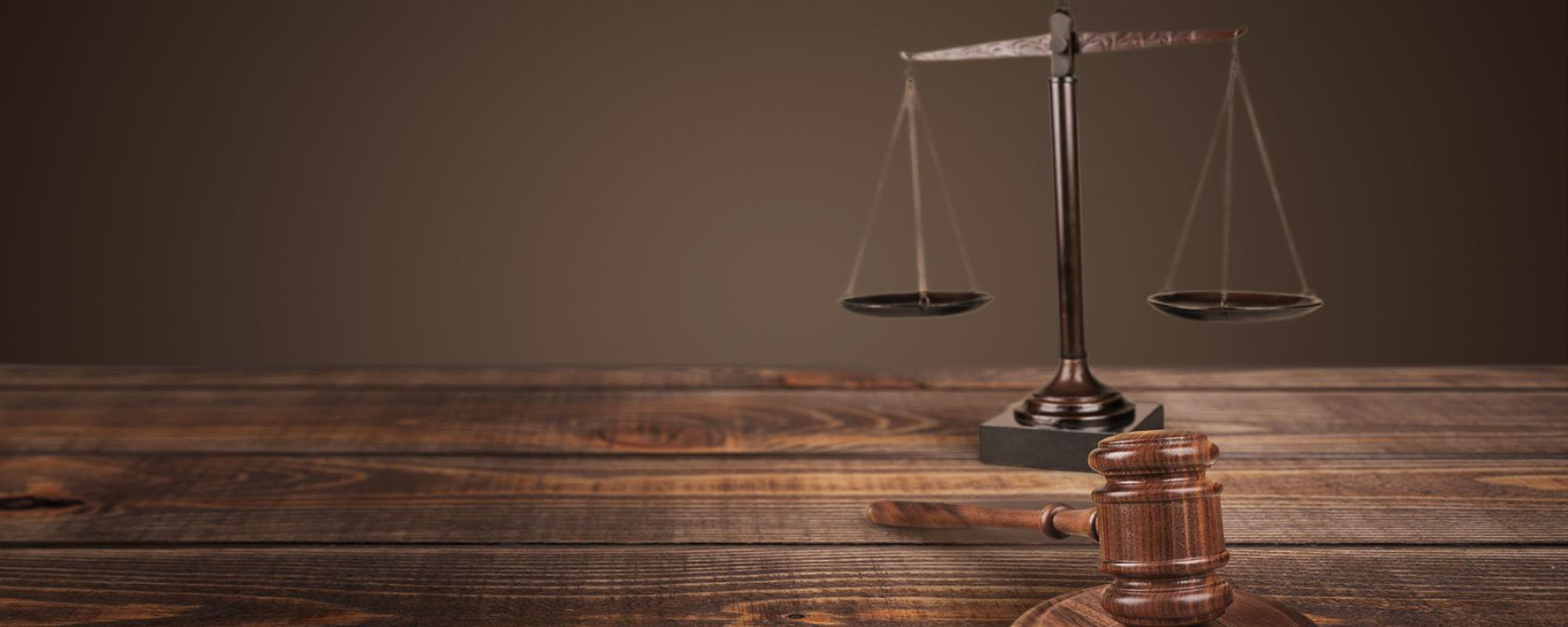 Wooden gavel in front of a bronze justice scale on a wooden table.